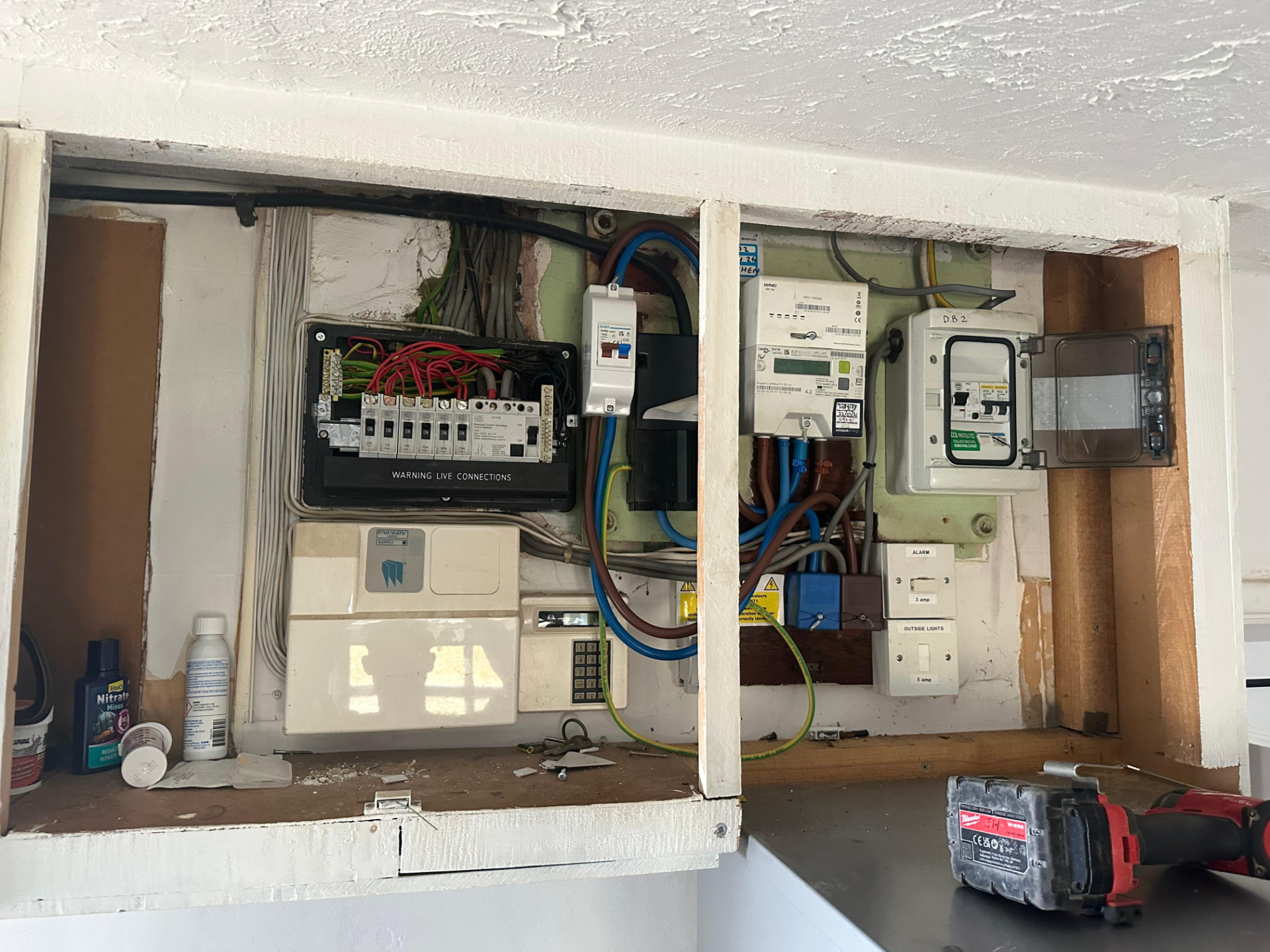 Old cluttered fuse box with alarm panel and exposed wiring before consumer unit upgrade