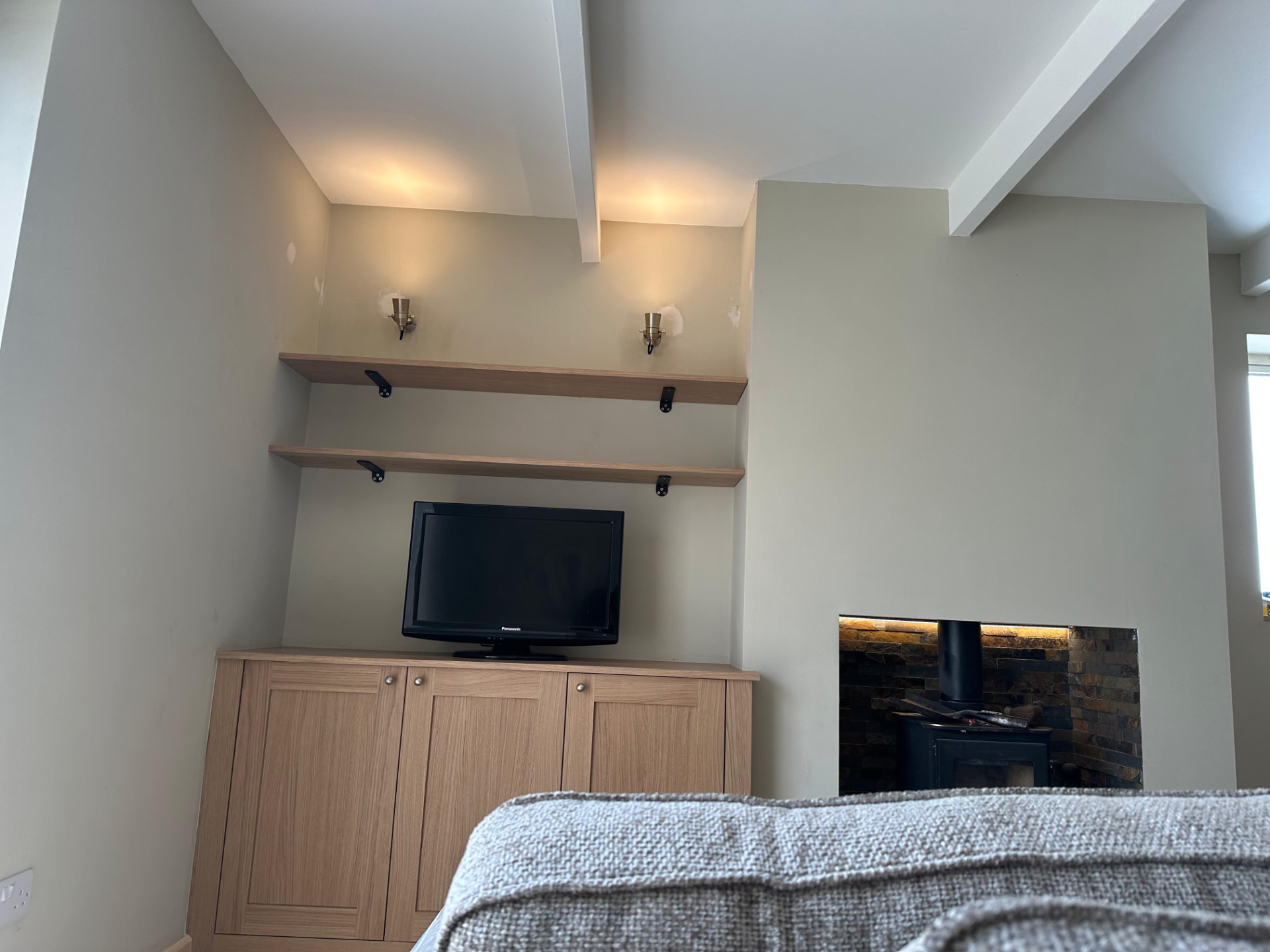 Living room fitted with warm accent wall lights above bespoke cabinetry and log burner