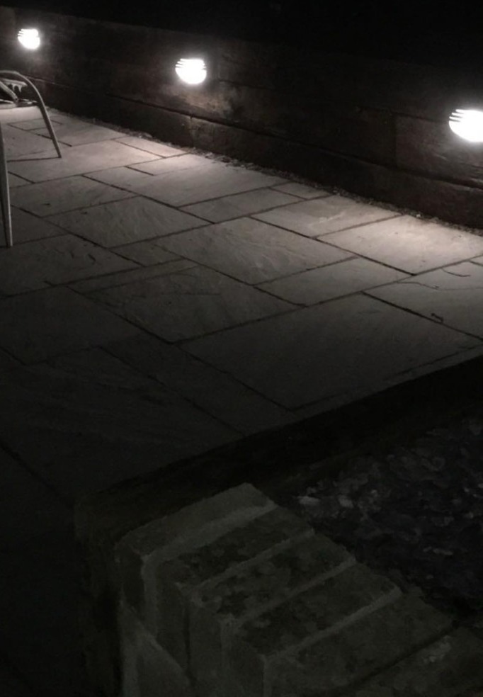 External patio wall lights illuminating a stone garden path at night